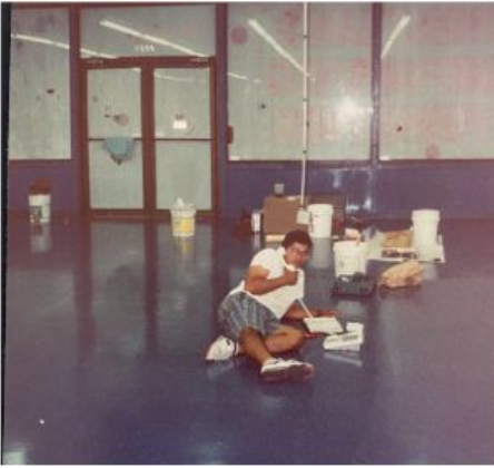 Person sitting on a floor with books and bags in a room with large windows.